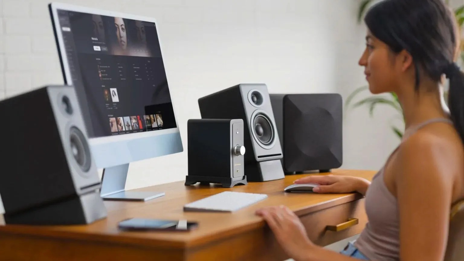 Person using a desktop computer with black speakers and audio equipment on a wooden desk.