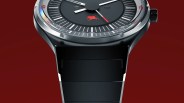 Close-up of a black watch face with white and red hands, a red Pegasus logo, and a black metal strap against a dark red background.