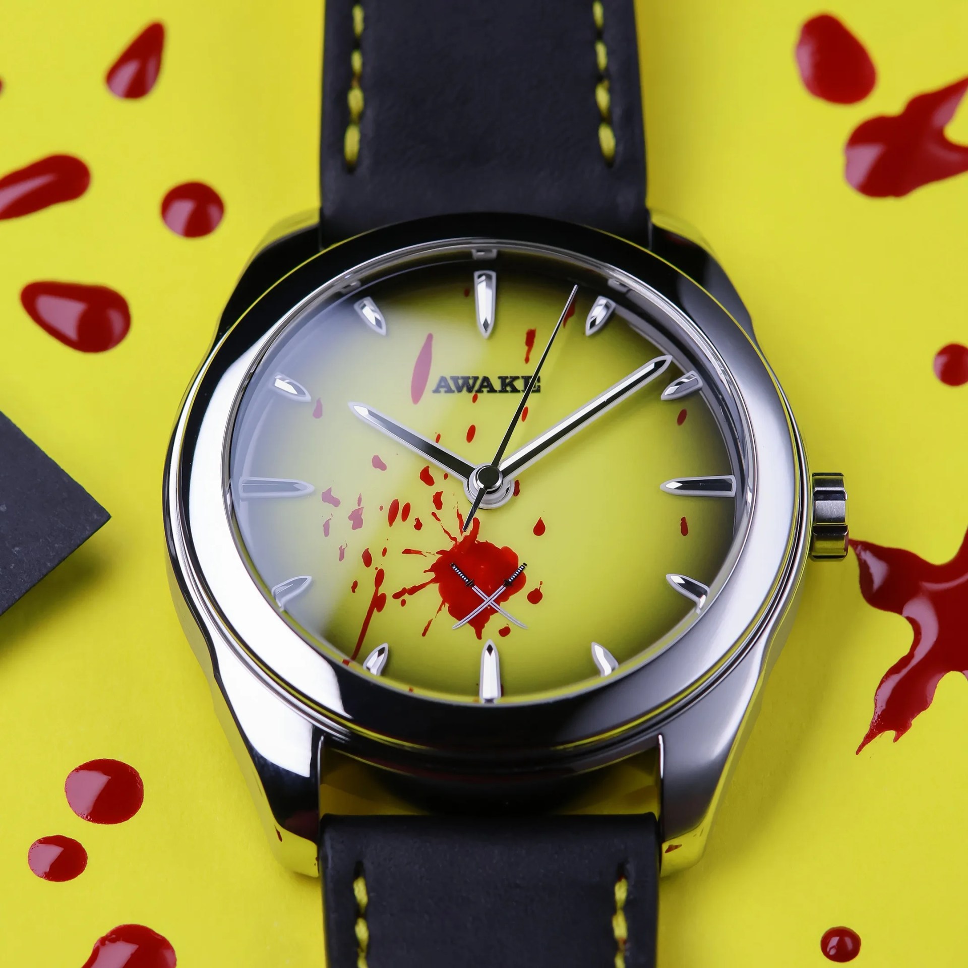 Silver wristwatch with yellow dial, black leather strap with yellow stitching, and red paint splatters on dial and background.