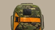 Green and brown camouflage backpack with orange strap and black buckle on a beige background.