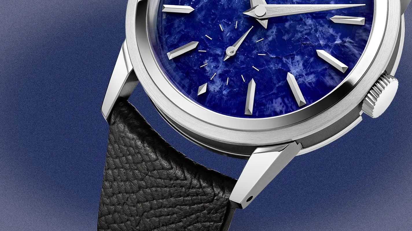 Close-up of a wristwatch with a textured deep blue dial, silver hour markers, and a black leather strap.