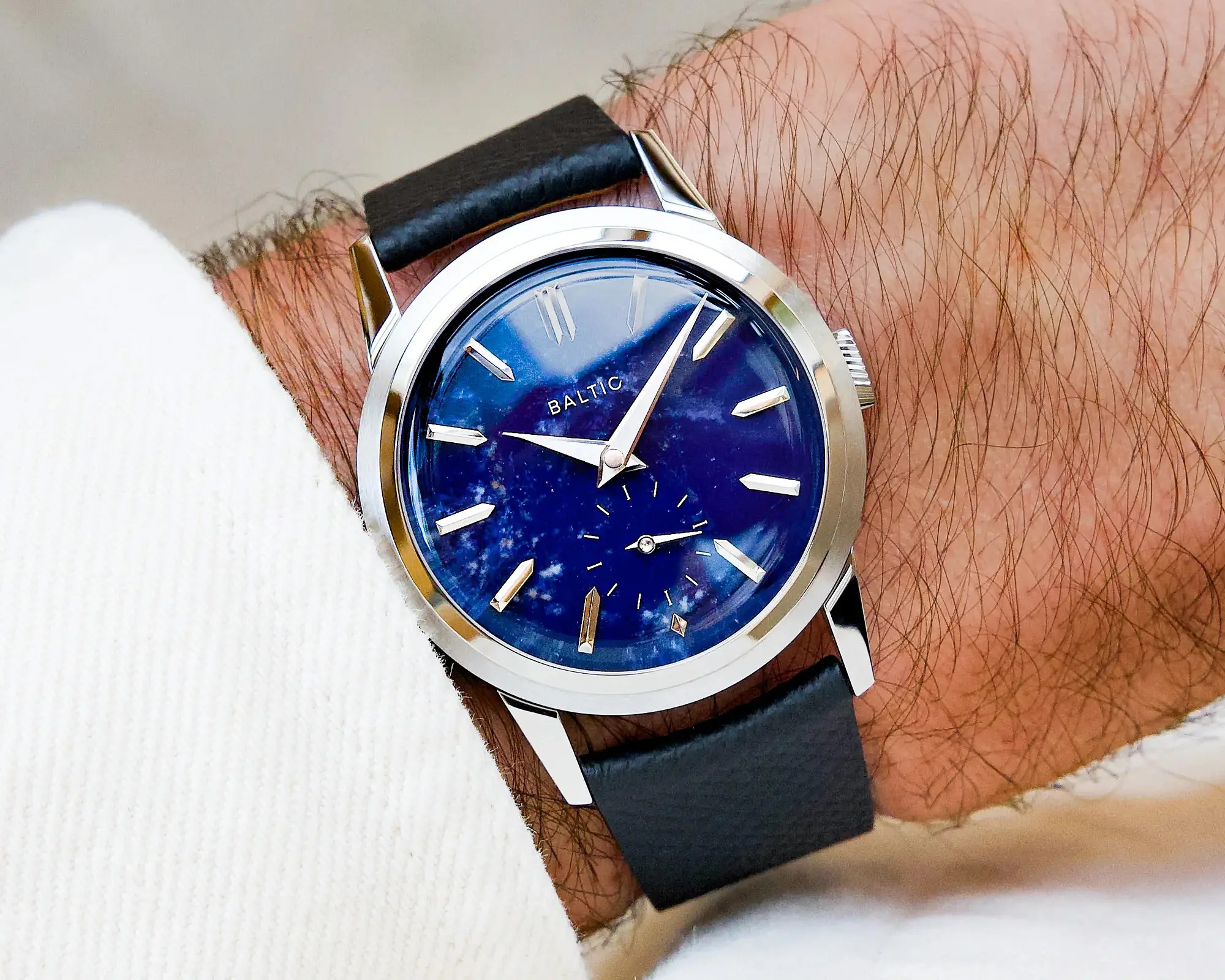Wristwatch with a polished silver case, deep blue dial, silver hour markers, and black leather strap worn on a wrist.