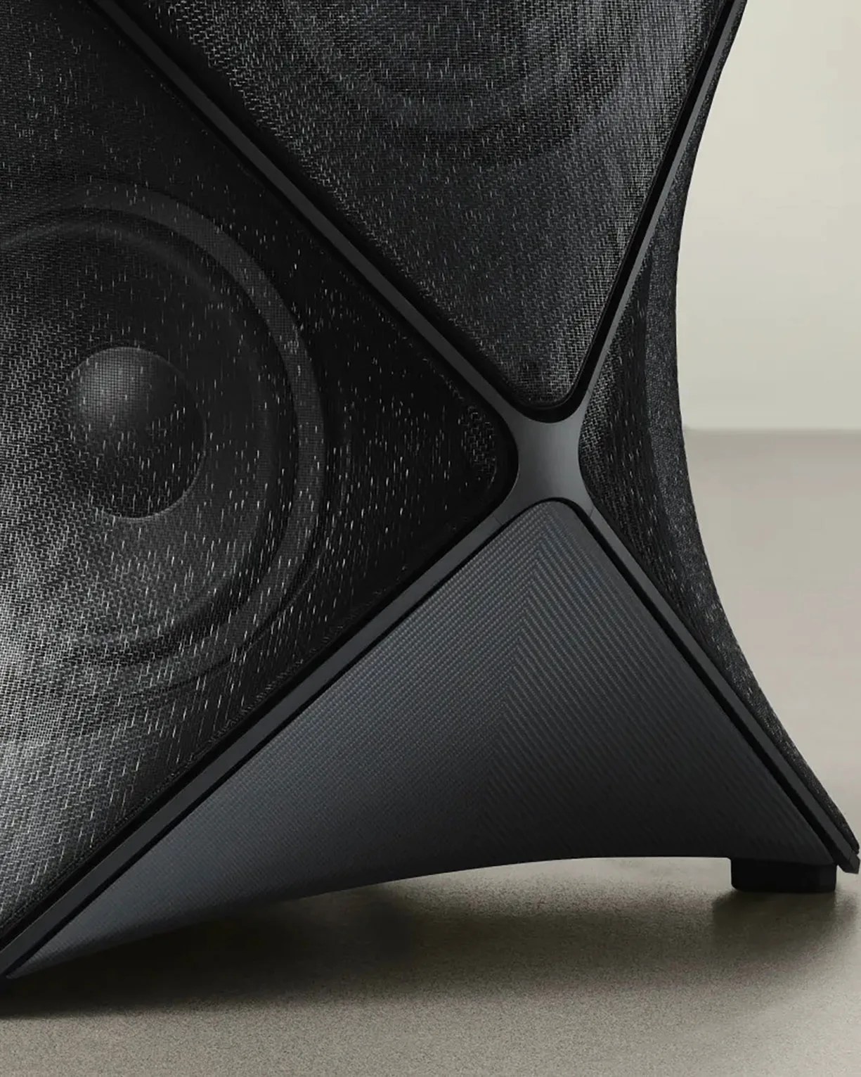 Close-up of a black speaker with a mesh cover and a triangular base on a gray surface.