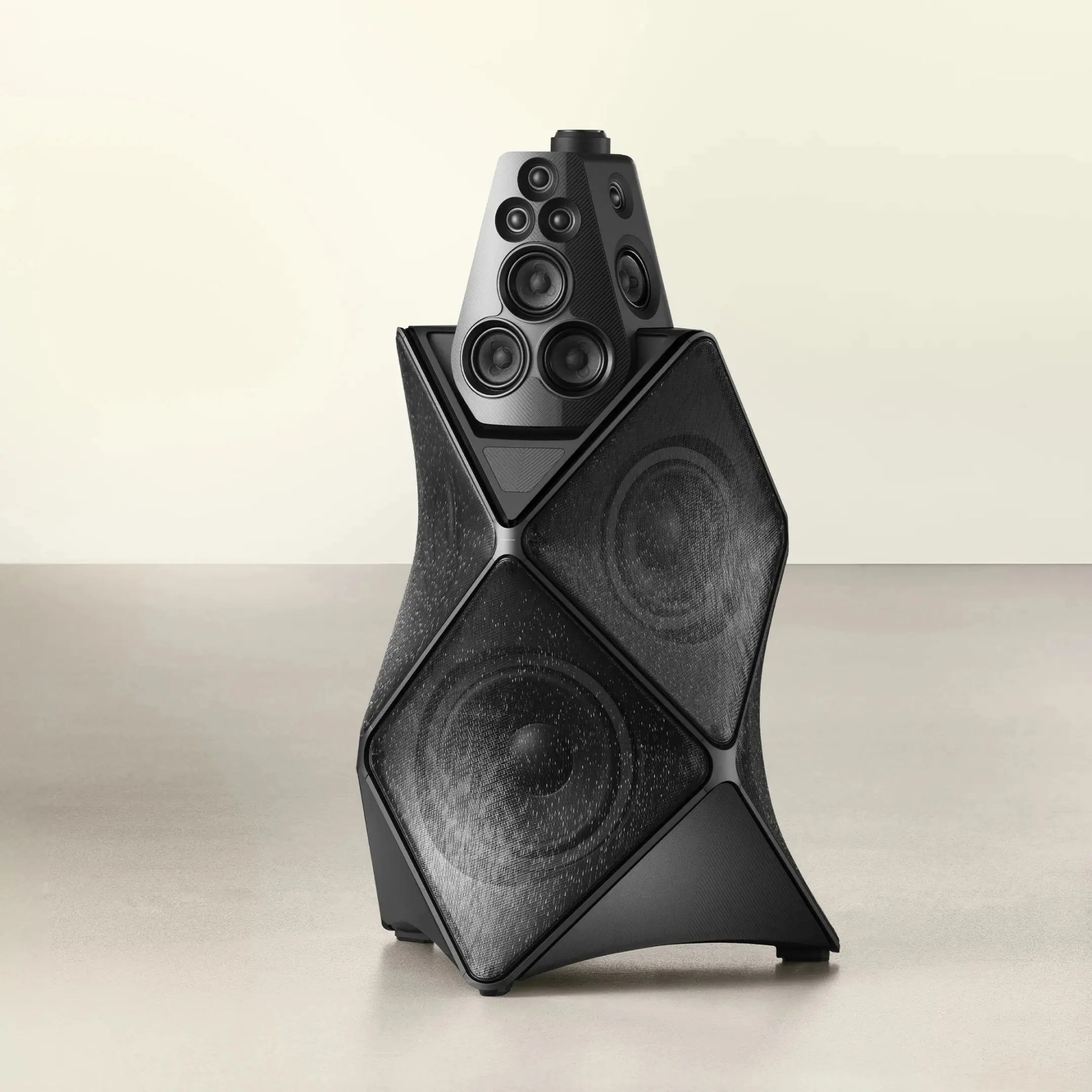 Black and gray multi-driver speaker with a geometric, angular design on a beige surface.
