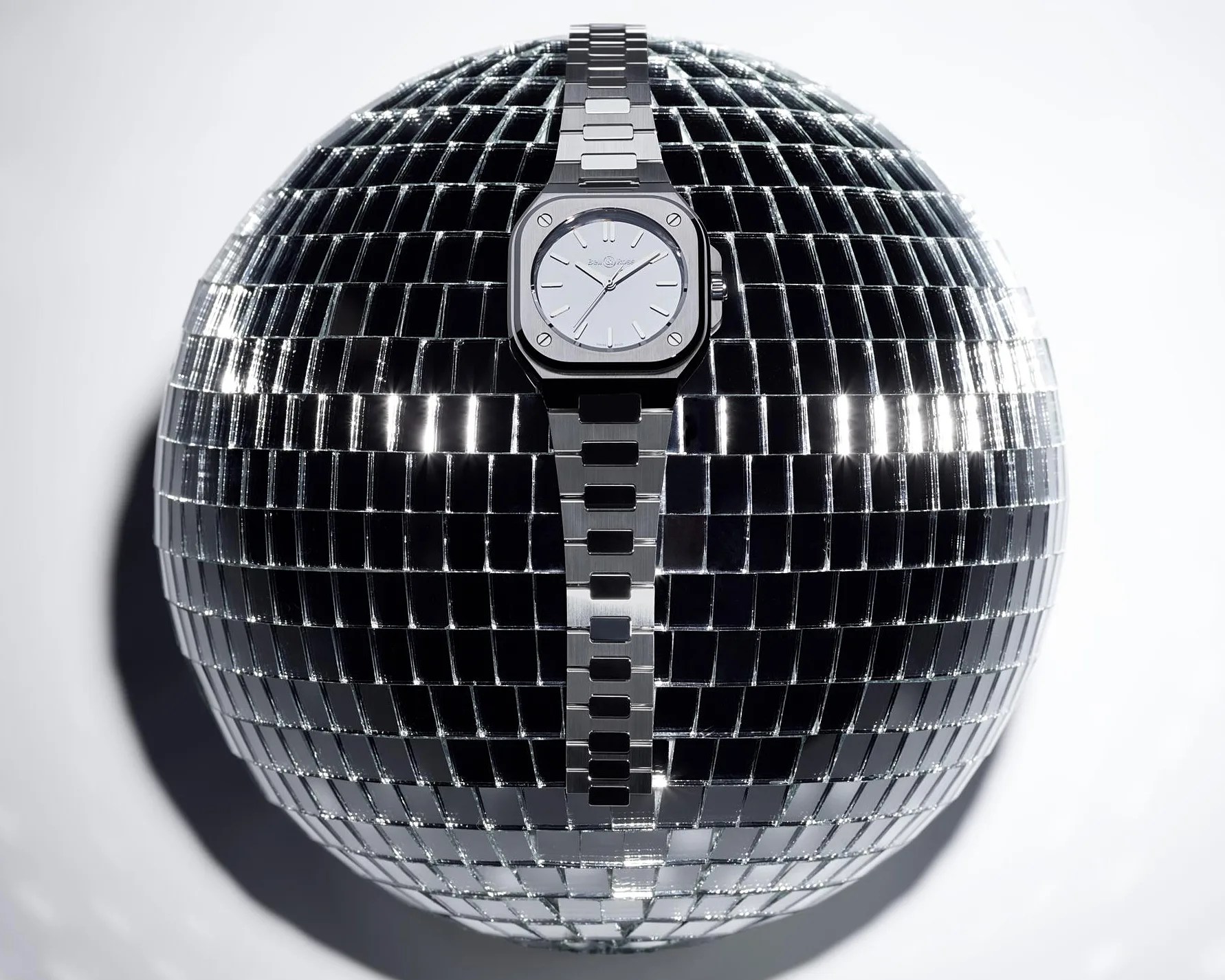 Silver metal wristwatch with a square face and white dial placed vertically on a reflective disco ball.