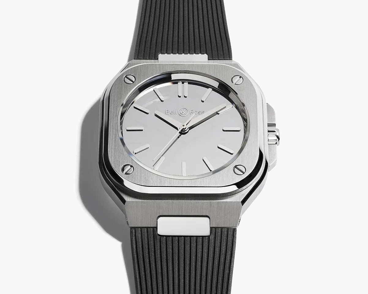 Square stainless steel Bell & Ross wristwatch with a white dial and black ribbed rubber strap.