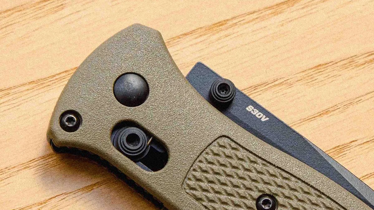 Close-up of a folding knife handle with textured olive green grip and partially visible black blade marked "S30V.