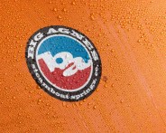 Close-up of an orange fabric with water droplets and a circular "Big Agnes Steamboat Springs CO" logo in red, white, blue, and black.