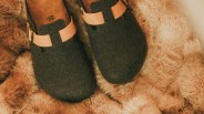 Pair of dark gray felt clogs with tan leather straps resting on a light brown fur rug.