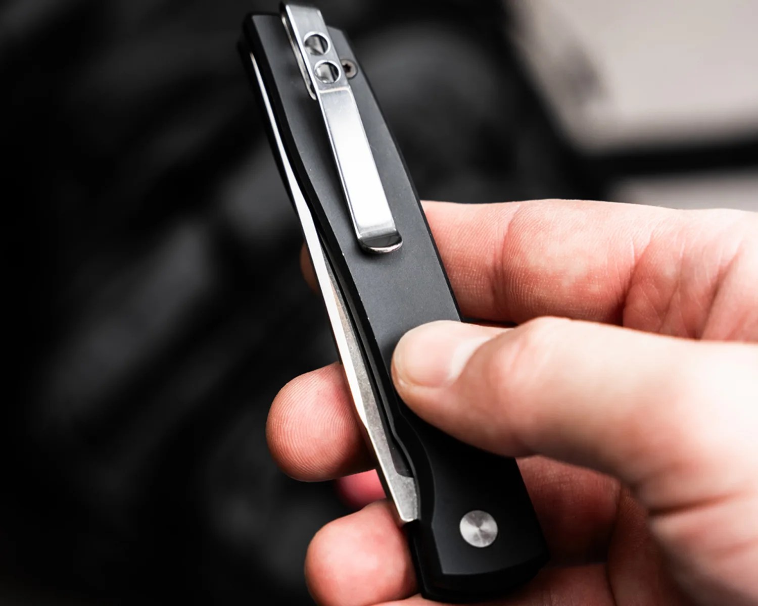 Hand holding a closed black folding pocket knife with a silver clip.