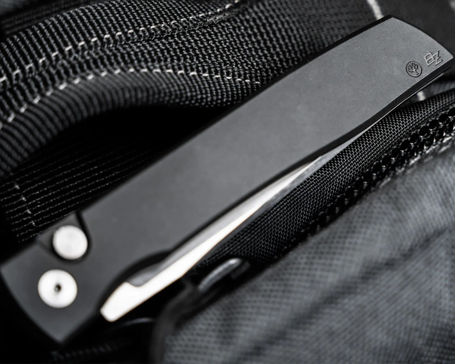 Black folding knife with metal clip and textured handle resting on black fabric.
