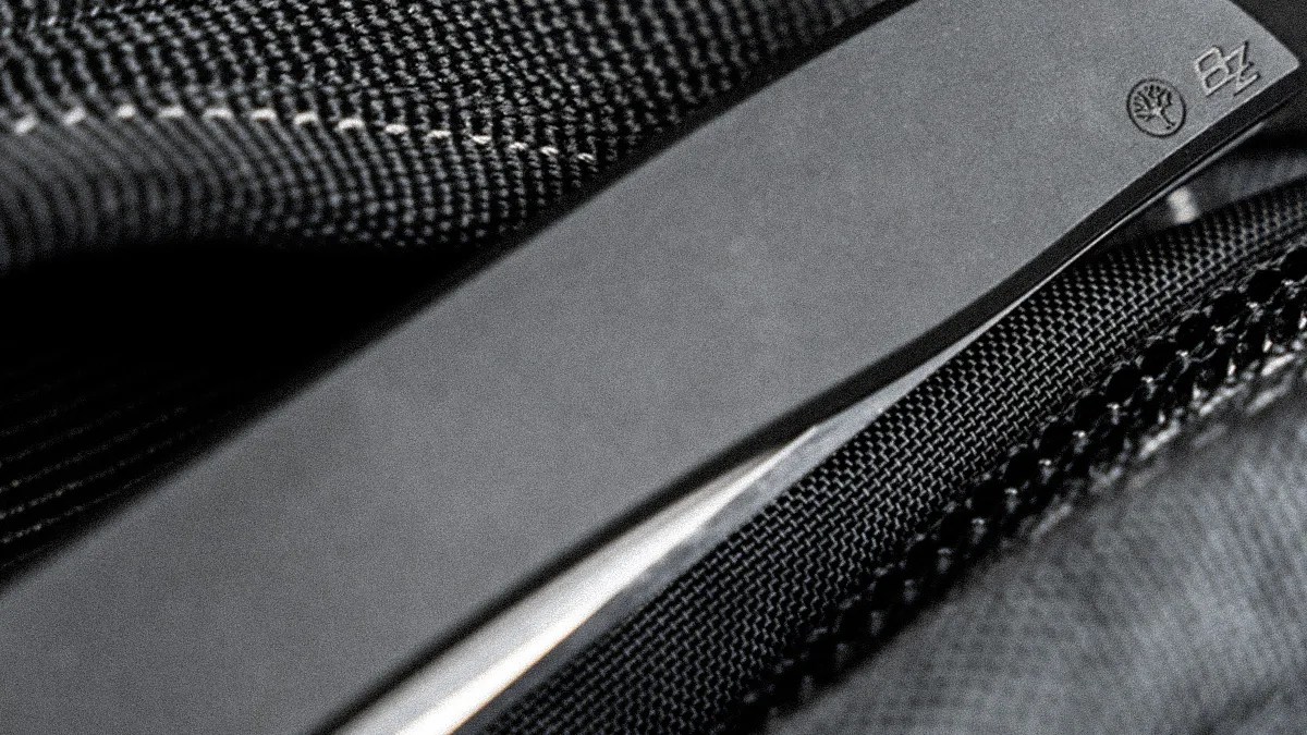 Close-up of a black folding knife blade with engraved logos resting on textured black fabric.