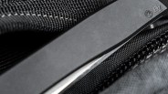 Close-up of a black folding knife blade with engraved logos resting on textured black fabric.