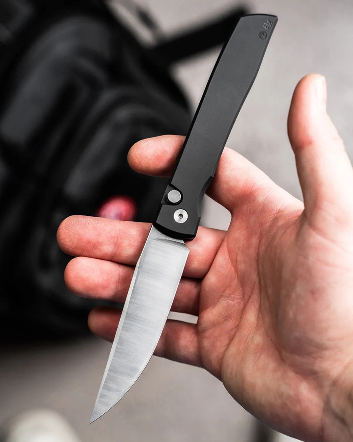 Hand holding a folding knife with a black handle and a stainless steel blade.
