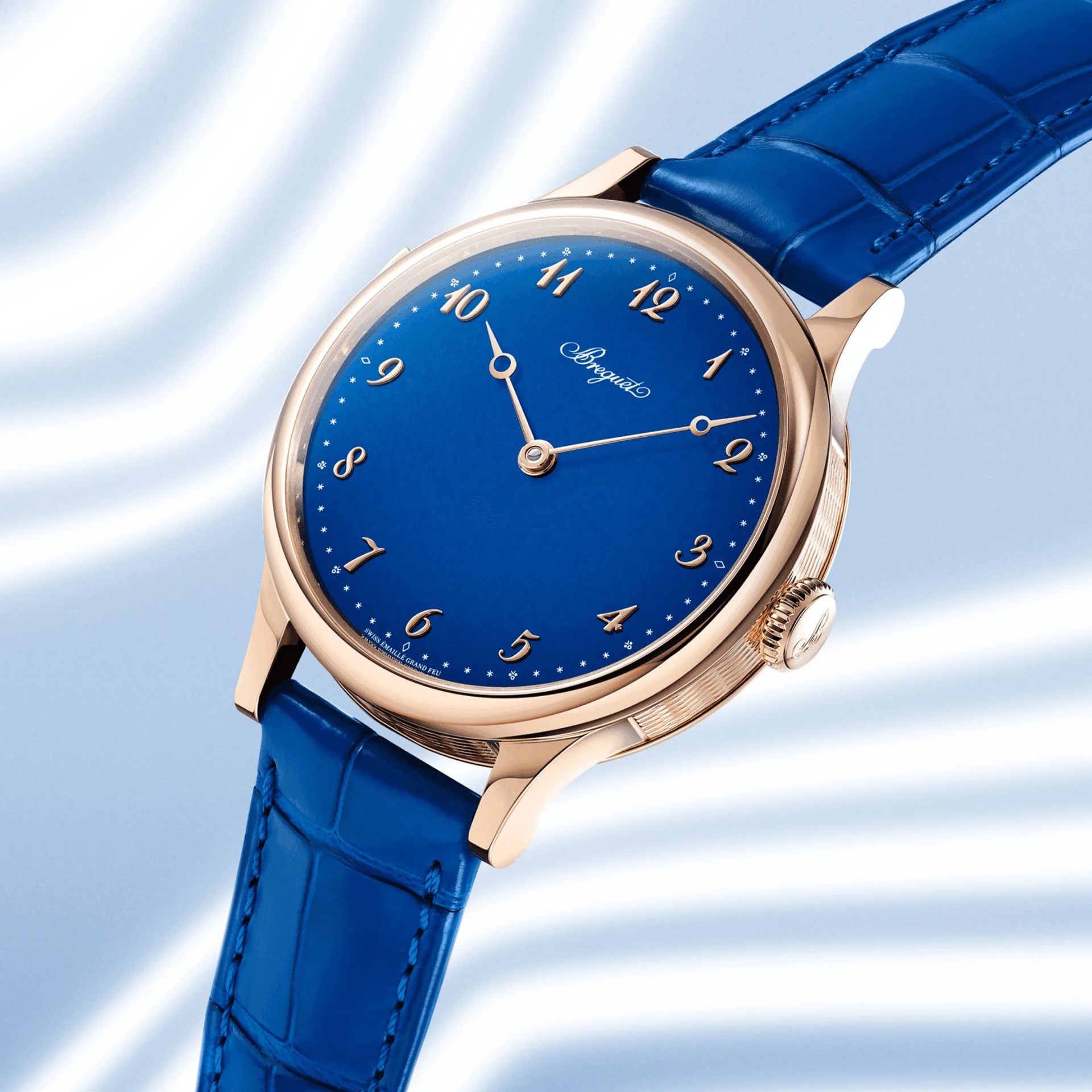 Rose gold wristwatch with a deep blue dial and matching blue leather strap on a light blue background.