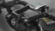 Black bicycle handlebar with mounted Garmin GPS device, front light, and attached handlebar bag.