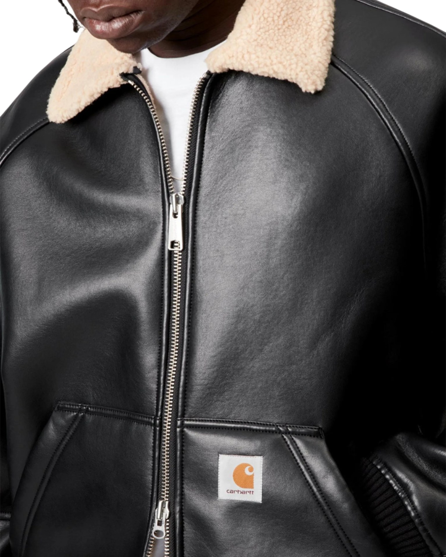 Black leather jacket with cream sherpa collar and front zipper, featuring a Carhartt logo patch on the pocket.