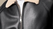 Black leather jacket with a silver zipper and beige sherpa collar worn over a white shirt.