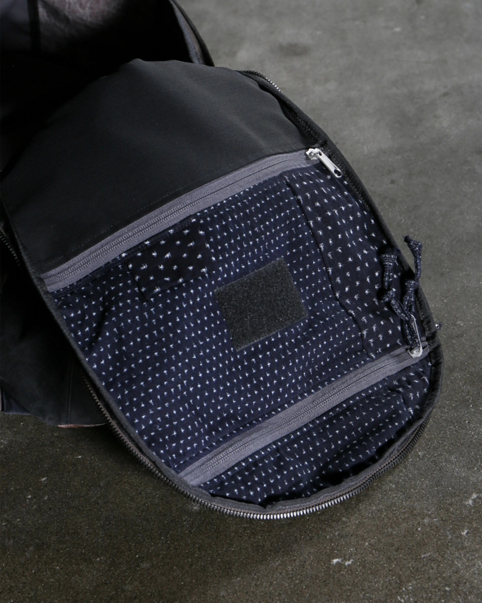 Interior of a black backpack showing a navy blue fabric lining with small white patterns and two gray zippered pockets.