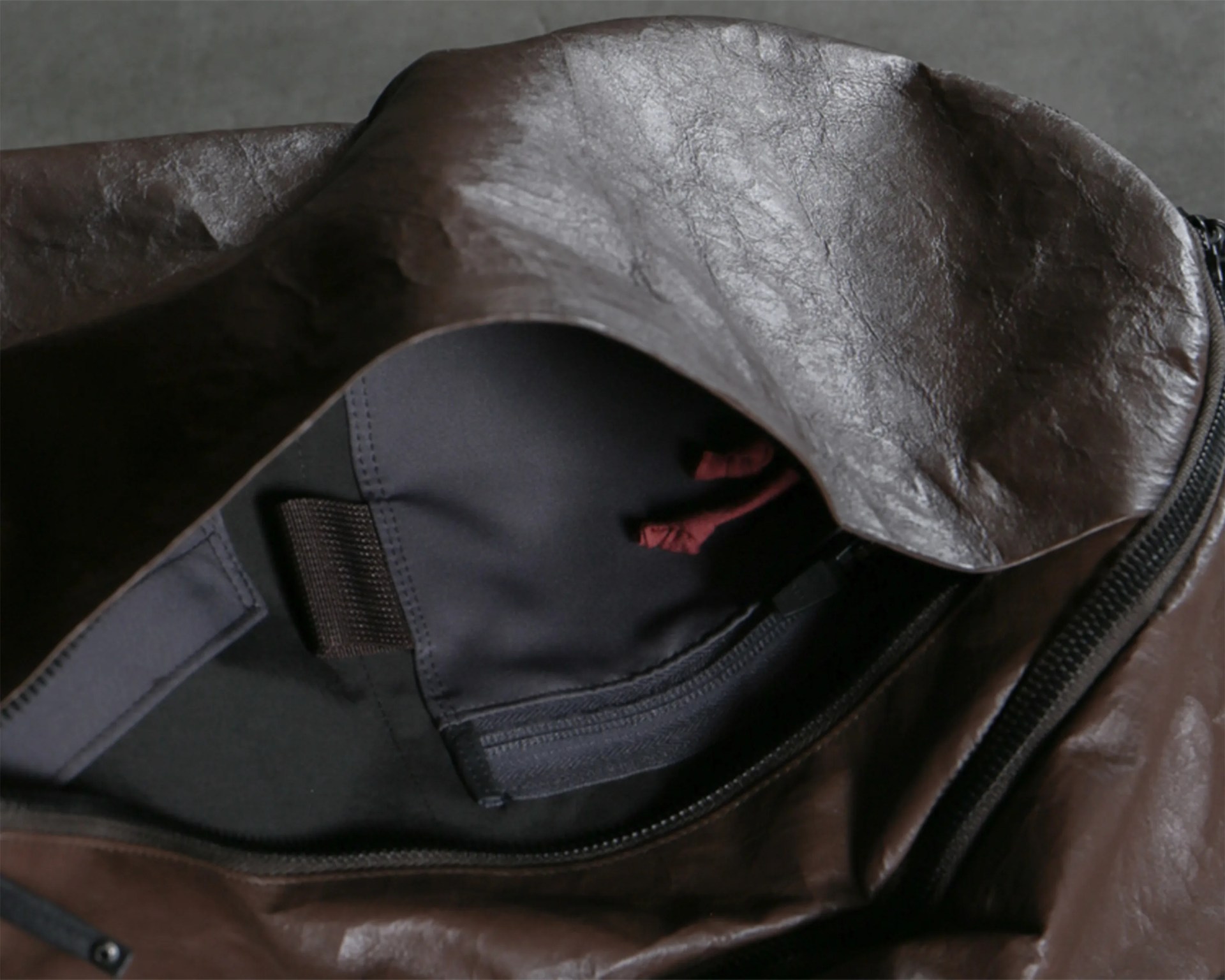 Close-up of a partially open dark brown leather bag showing a black fabric interior with a zipper and red drawstrings inside.