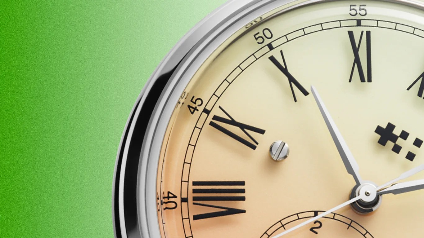 Close-up of a round watch with Roman numerals and silver frame against a green background.