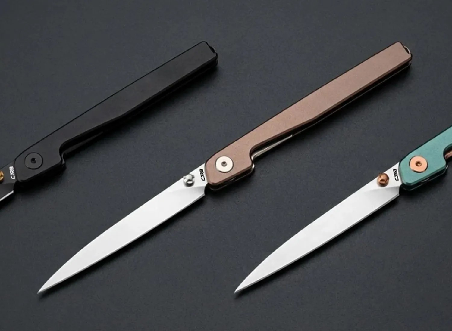 Three slim folding knives with straight-edged silver blades and handles in black, bronze, and teal colors on a dark surface.
