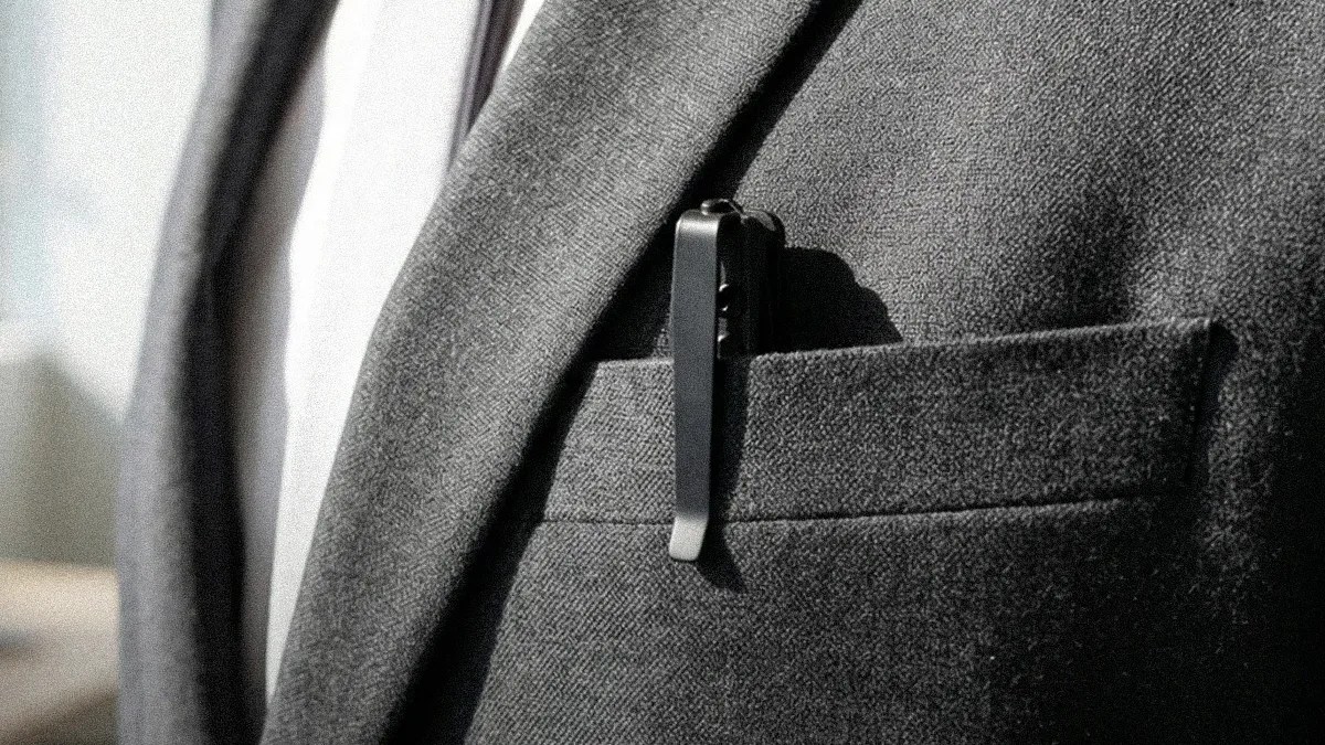 Black metal pen clipped to the pocket of a gray textured blazer worn over a white shirt.