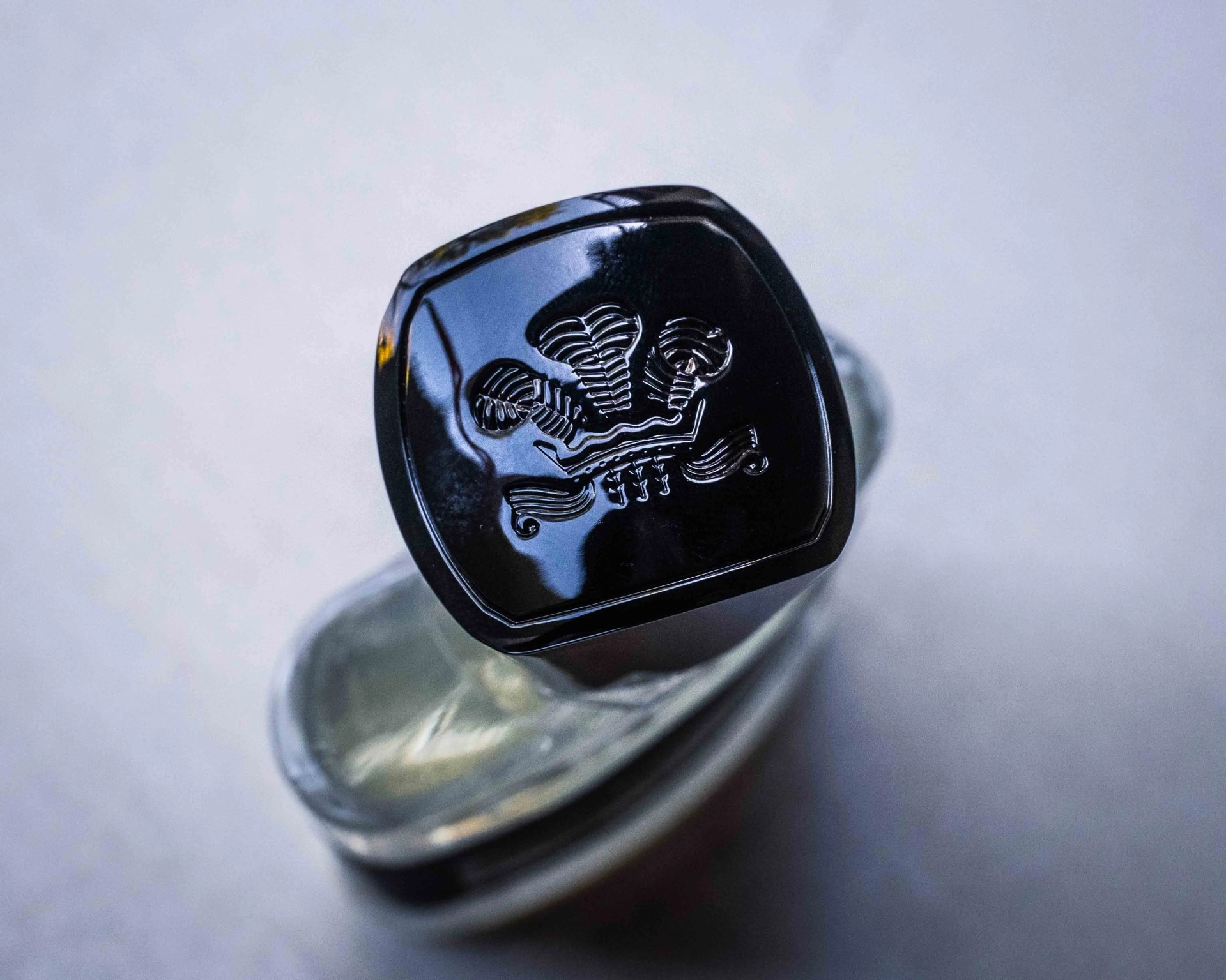 Black square bottle cap with an embossed crown design on a clear glass bottle.