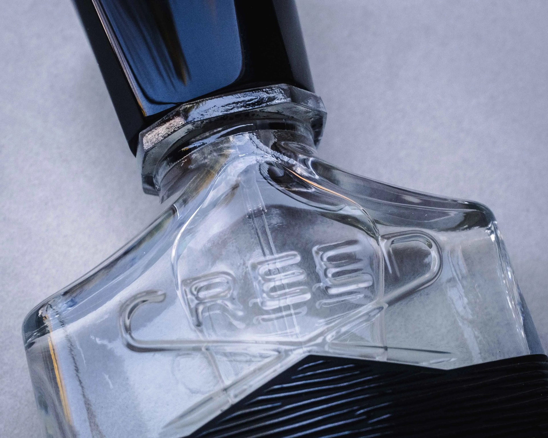 Close-up of a clear glass bottle with the word "CREW" embossed on it and a black cap.