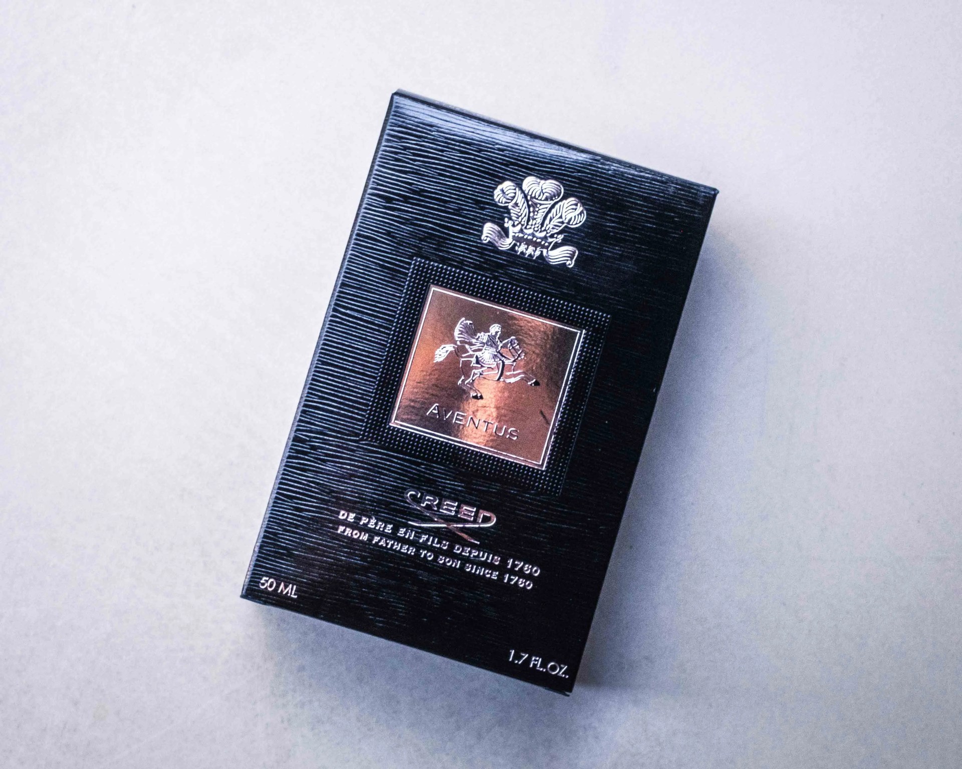 Black textured box of Creed Aventus perfume with silver horse emblem and text on a light surface.
