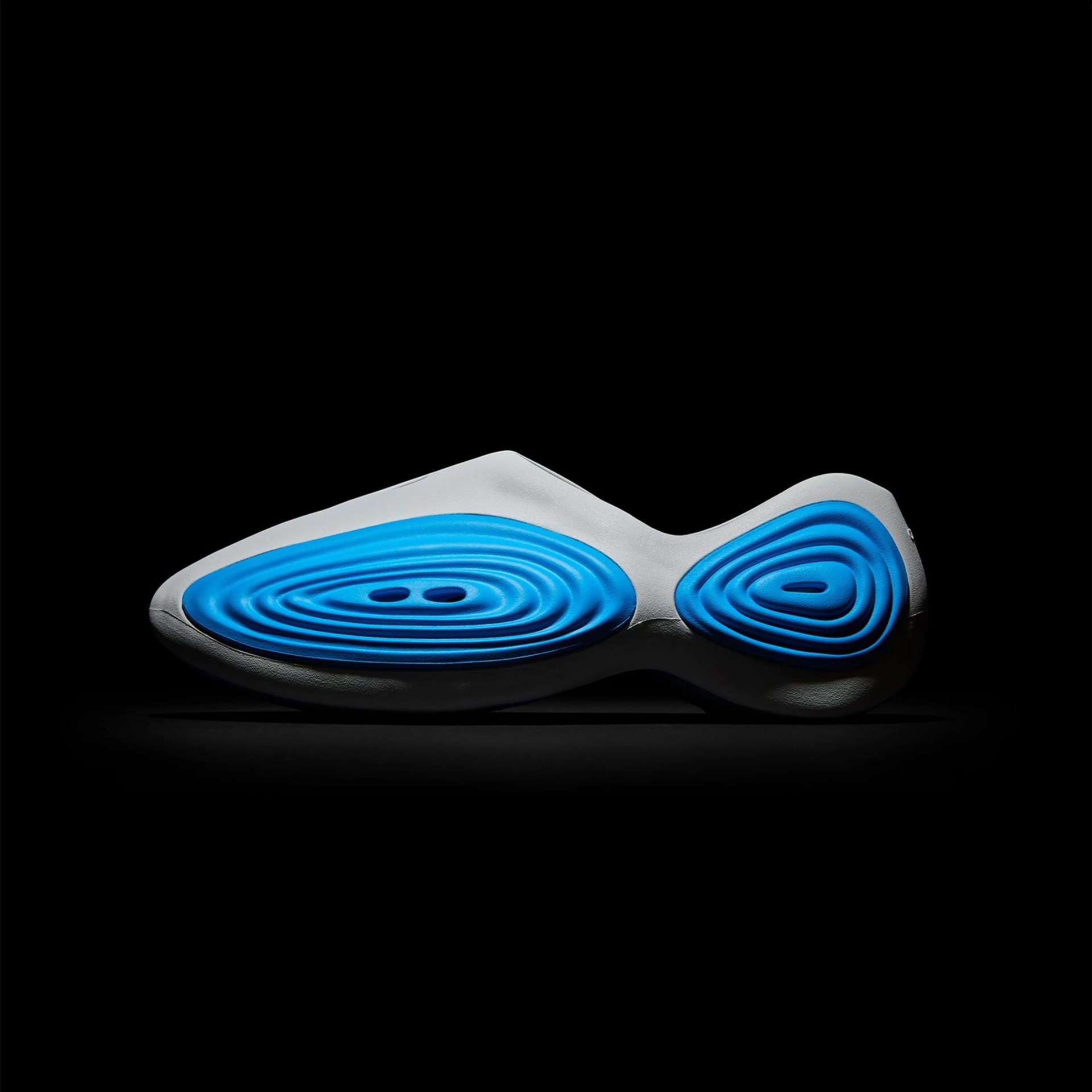 Gray and blue contoured shoe sole with concentric oval patterns on a black background.
