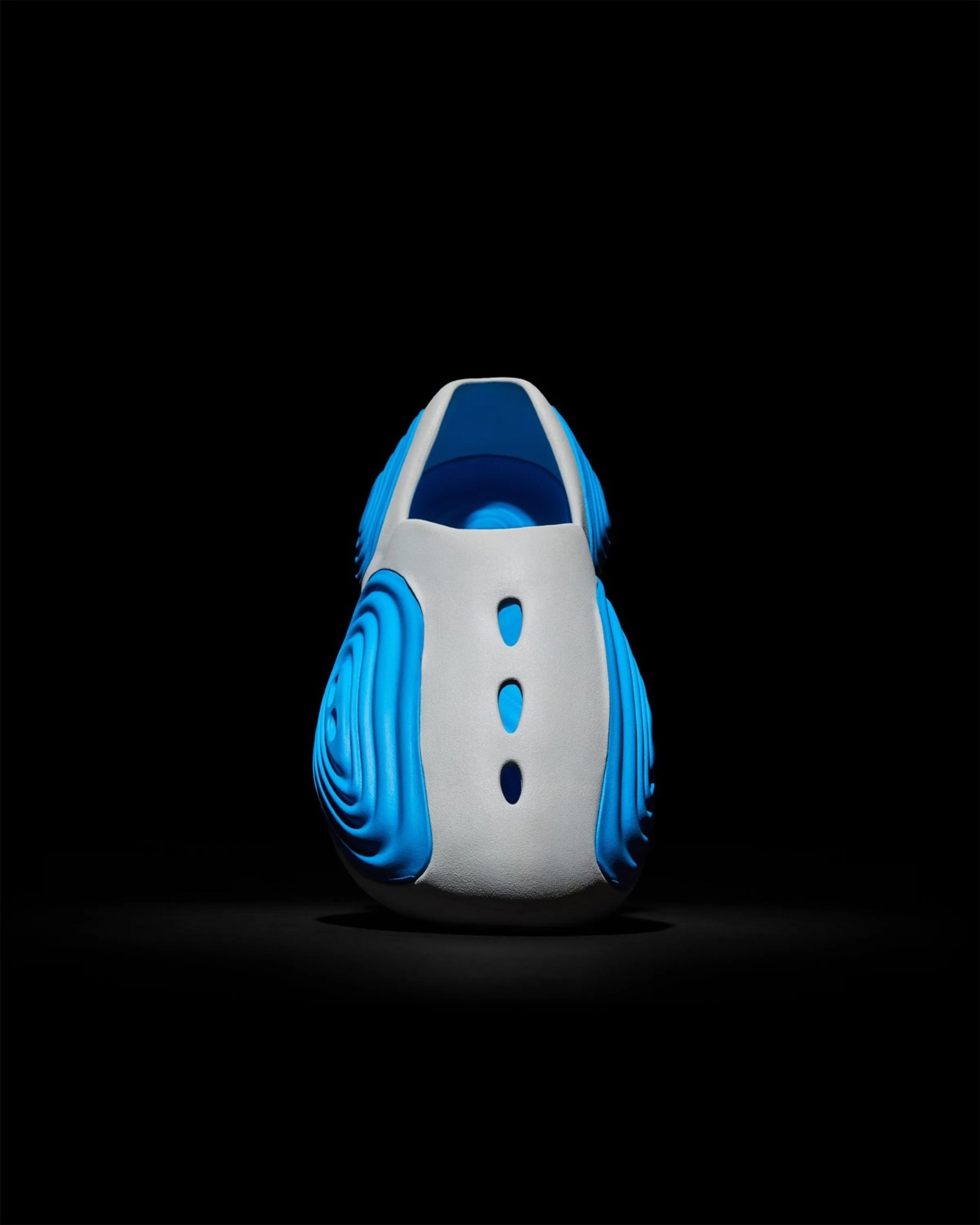 White and blue futuristic slip-on shoe with three ventilation holes on top, shown from the back on a black background.