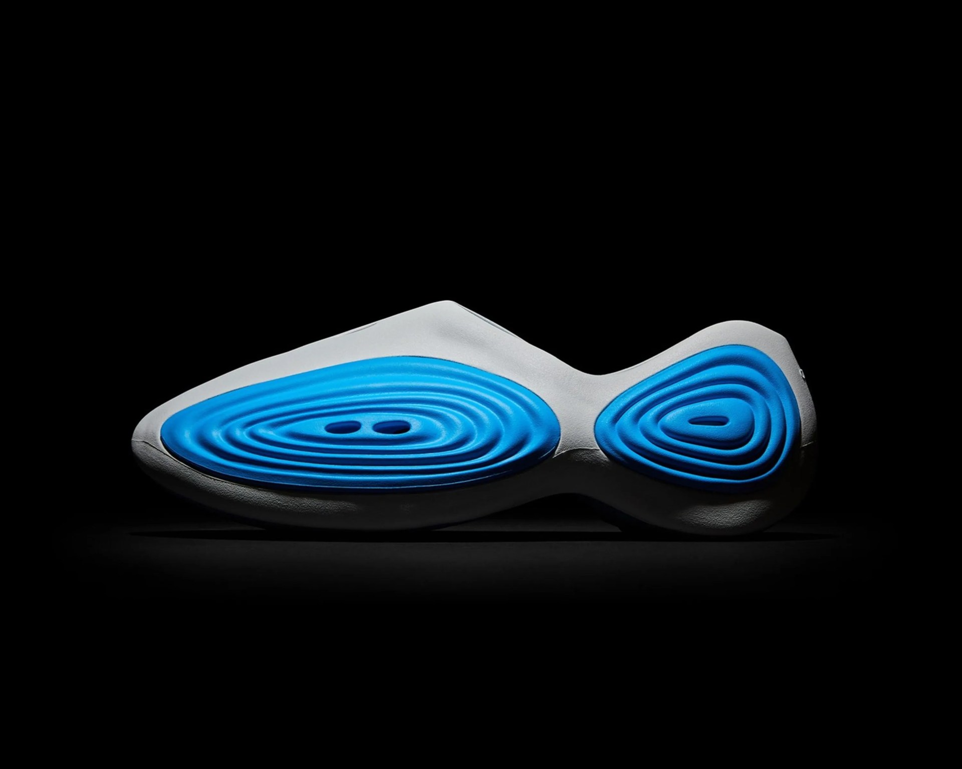 Side view of a white shoe sole with blue concentric oval patterns on a black background.