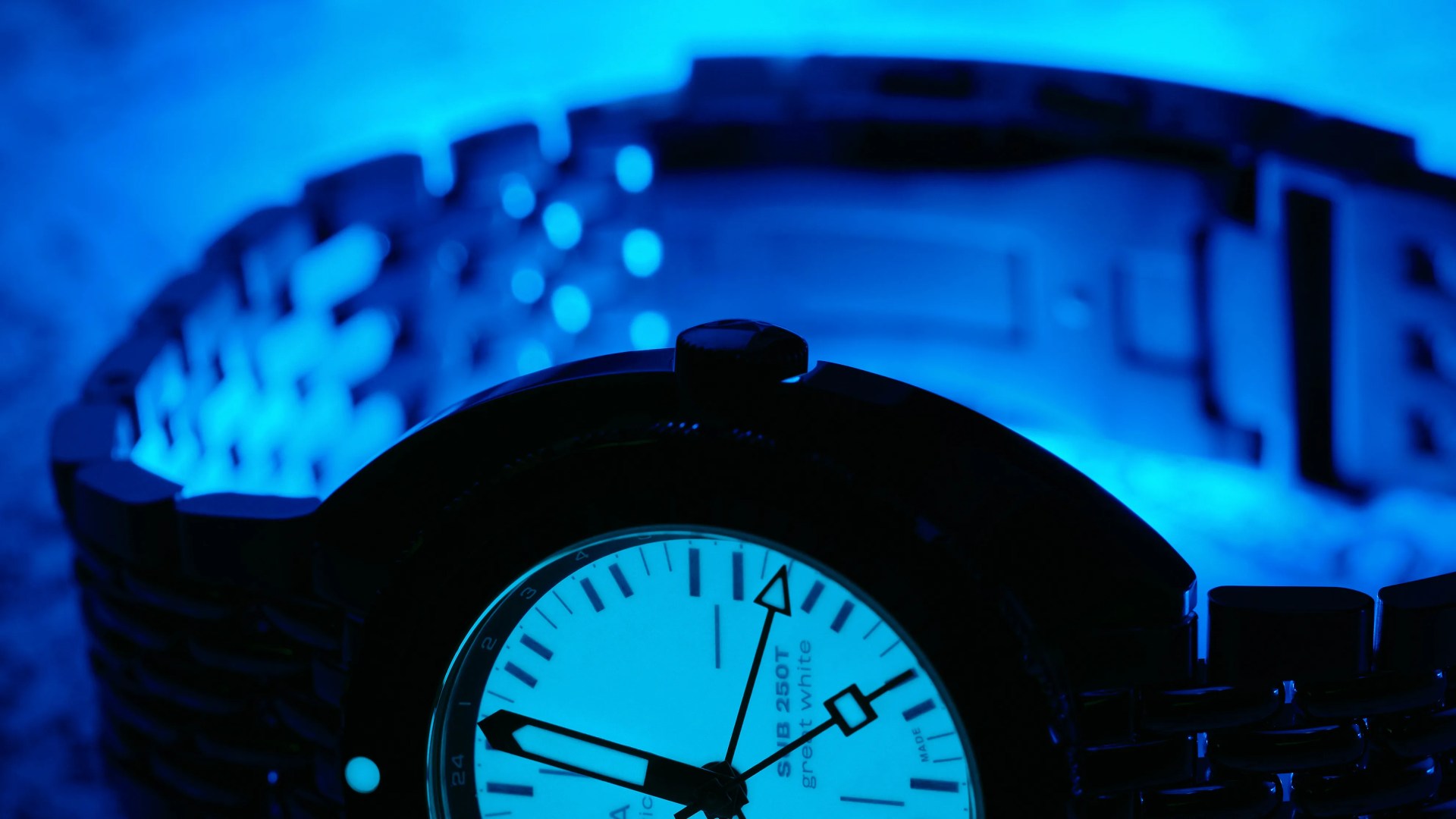 Close-up of a wristwatch with a metal band illuminated by blue light, showing the time around 9:50.