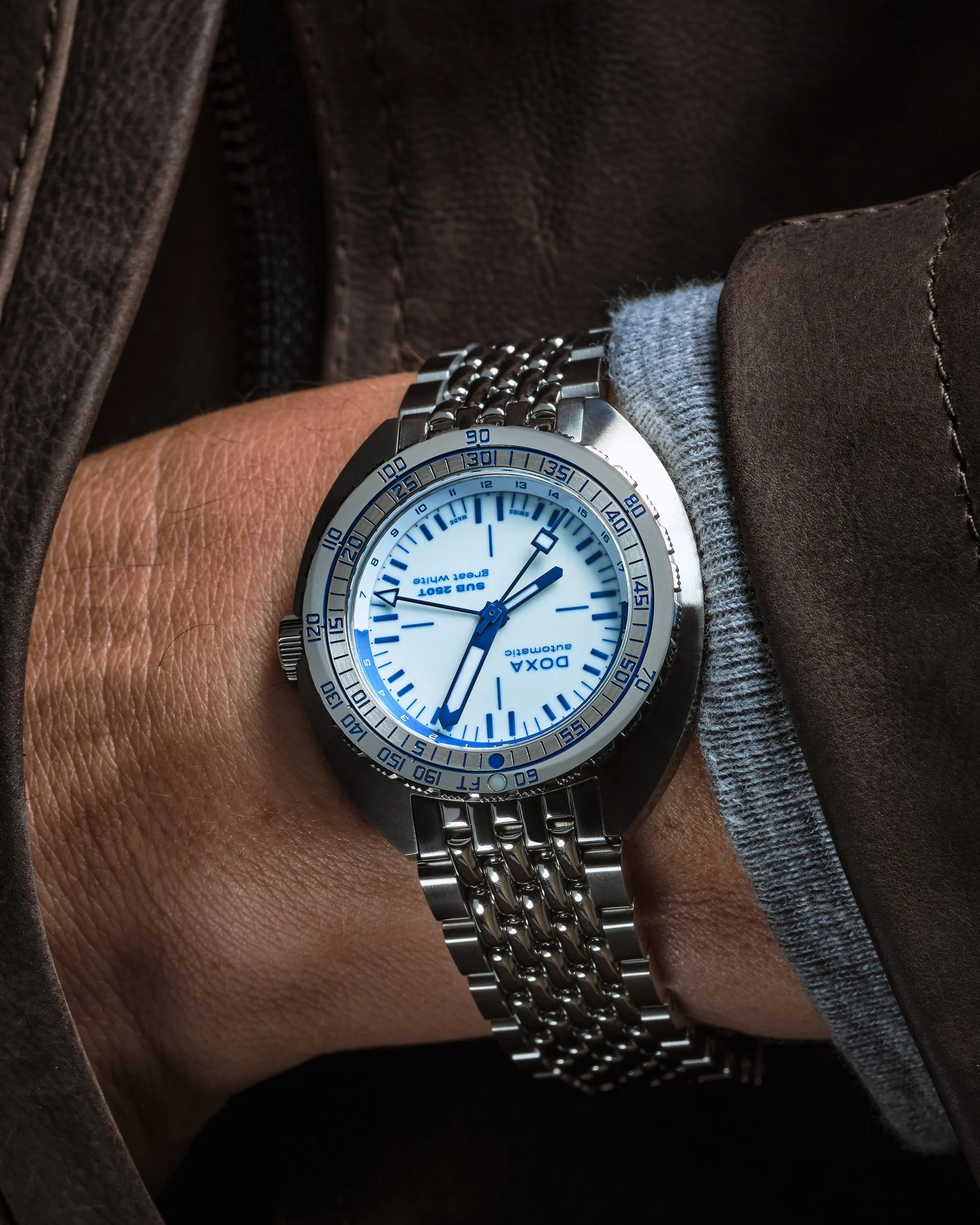 Silver DOXA SUB 250T wristwatch with white dial and blue markings on a metal bracelet worn on a wrist.