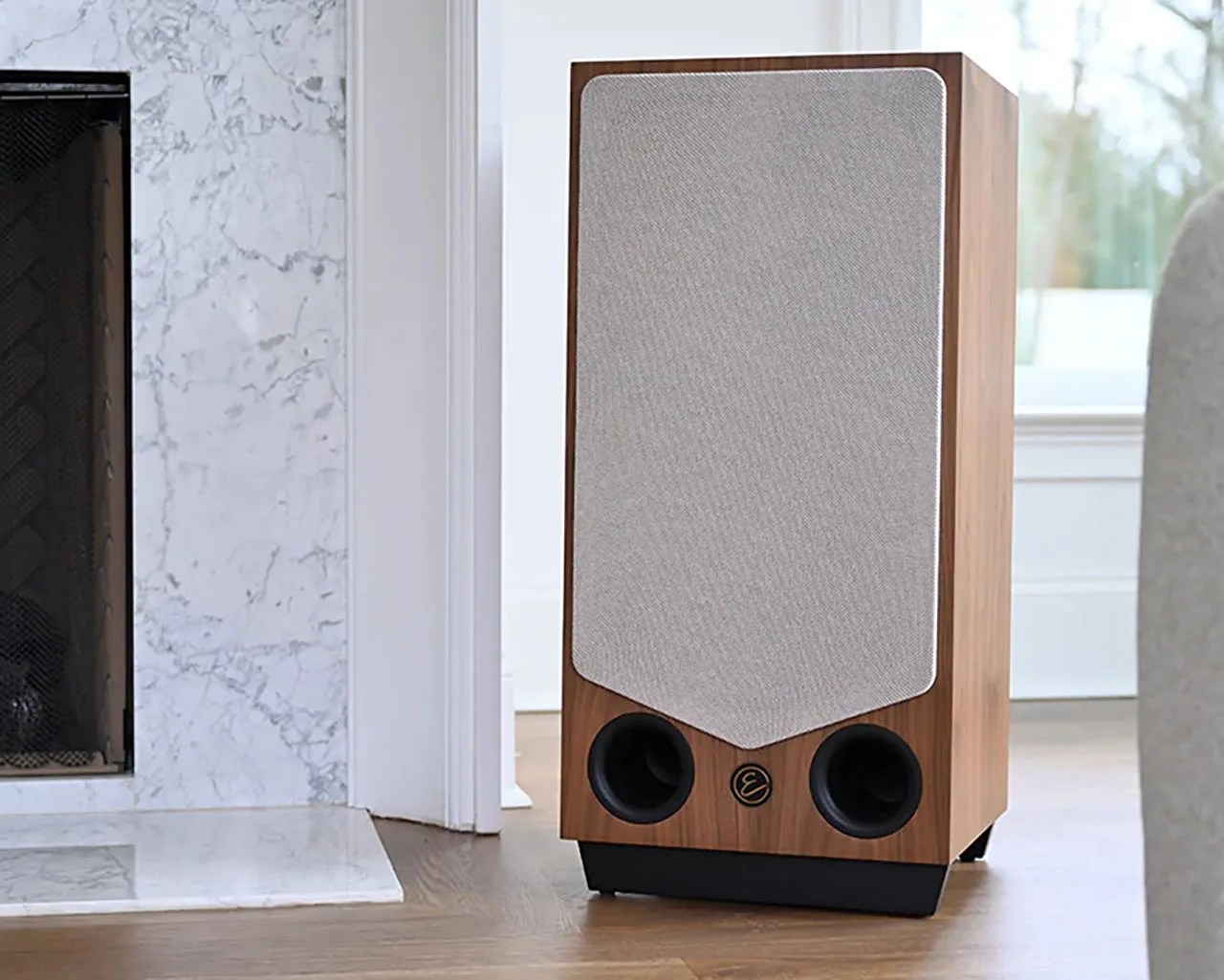 Tall wooden floor speaker with beige fabric grille and two black circular ports at the bottom.