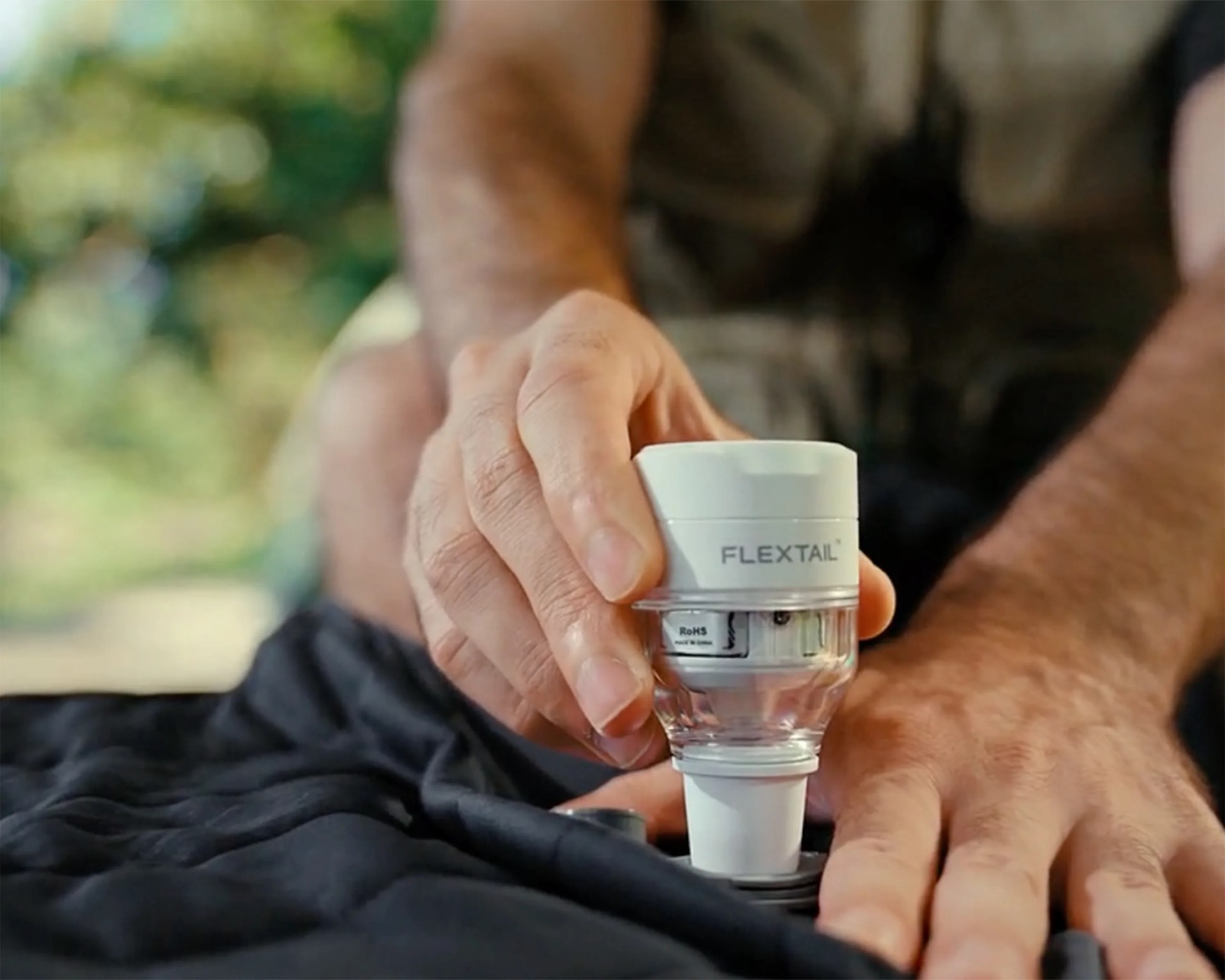 Hand holding a white and transparent FLEXTAIL device attached to black fabric.