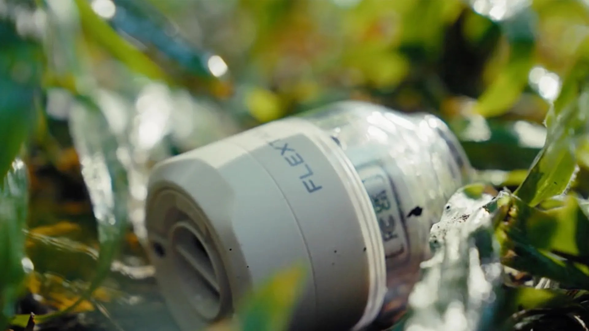 White plastic container labeled "FLEX" lying on grass with green leaves around it.