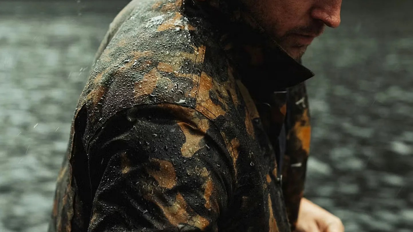 Close-up of a person wearing a wet camouflage jacket with water droplets on the fabric.