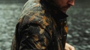 Close-up of a person wearing a wet camouflage jacket with water droplets on the fabric.