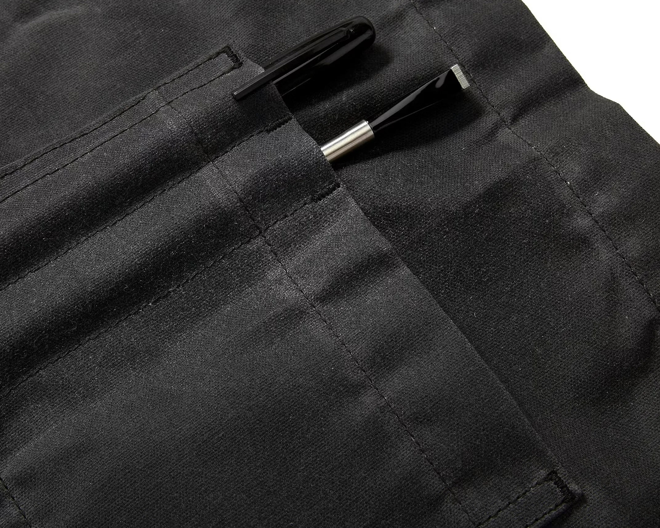 Two black pens in separate stitched pockets on black fabric.