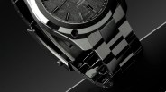 Close-up of a black watch bracelet with brushed and polished links on a dark reflective surface.