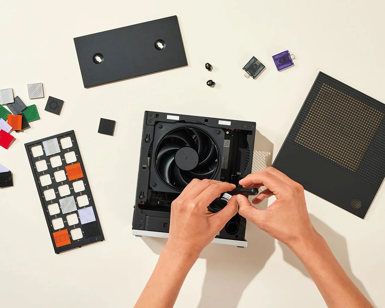 Hands assembling a small black computer with a visible cooling fan and colorful keycaps scattered nearby.