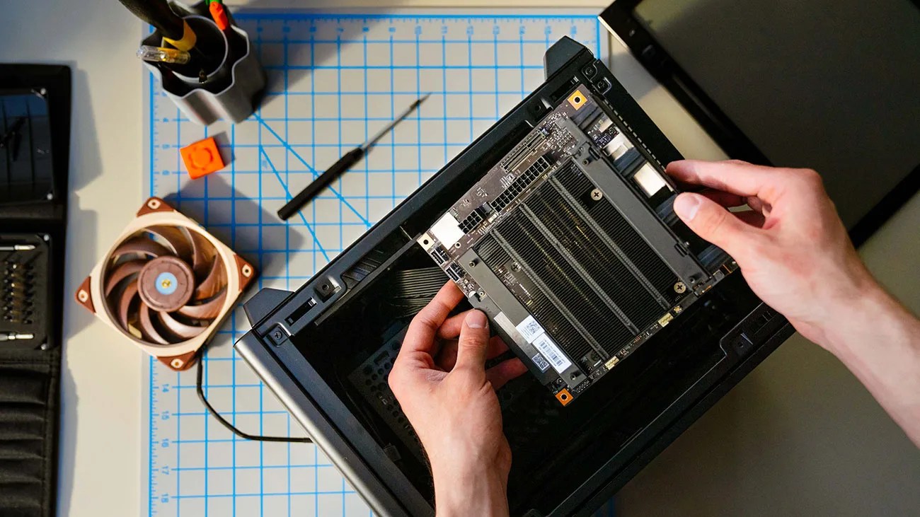 Hands installing a computer component inside a black PC case on a blue grid mat.