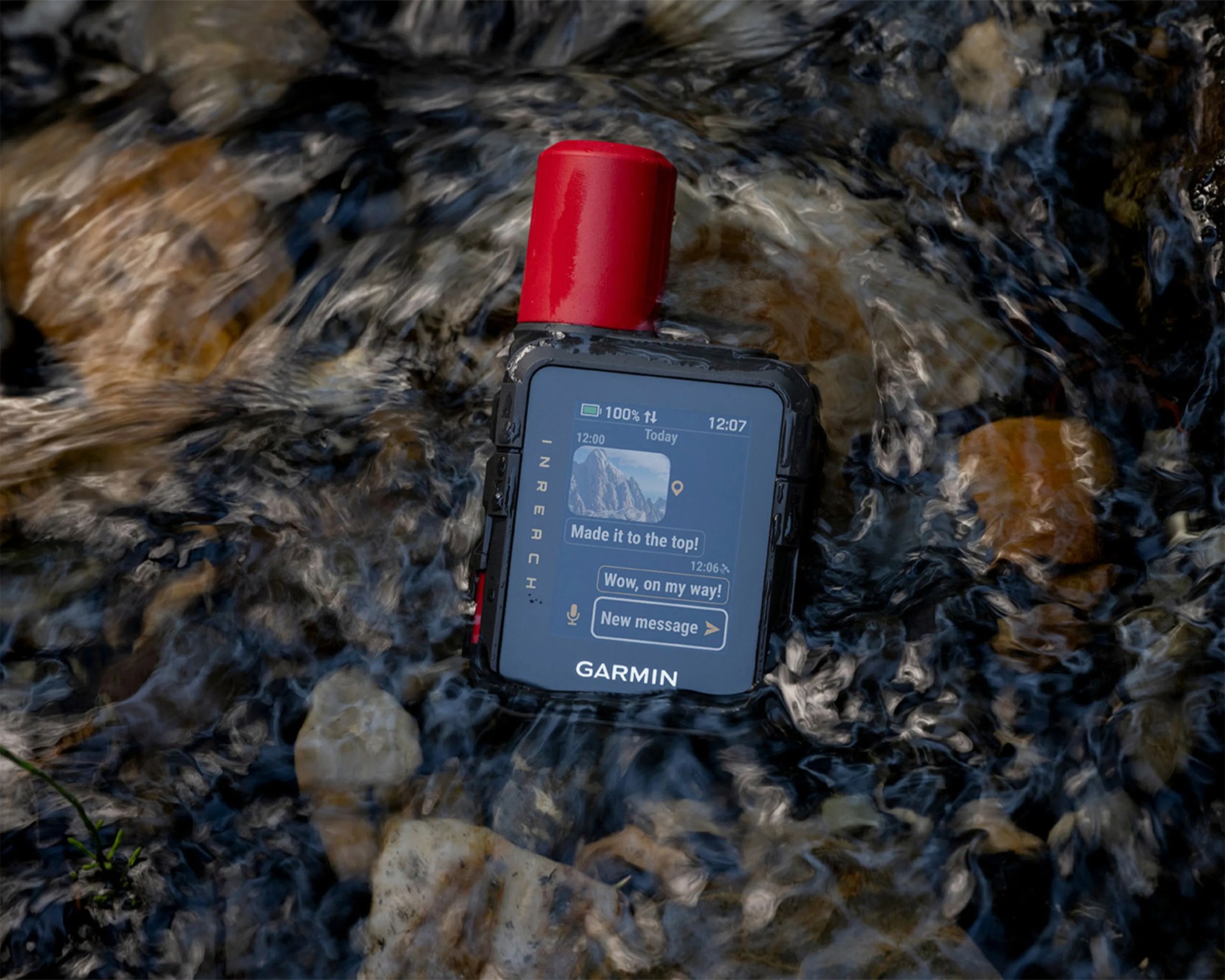Garmin InReach satellite communicator with red antenna submerged in flowing water over rocks.