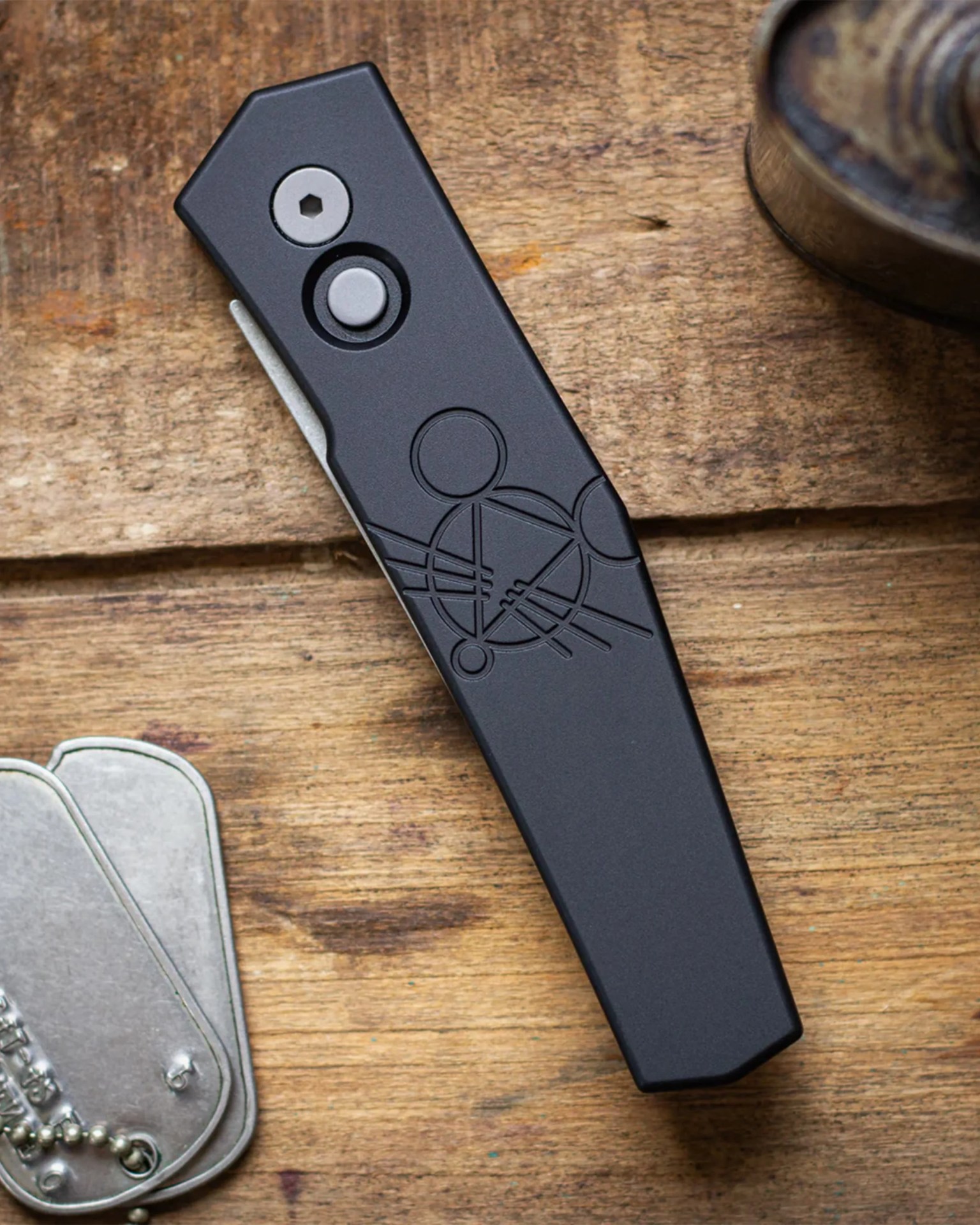 Black folding knife with geometric circle and line design on handle, resting on a wooden surface.