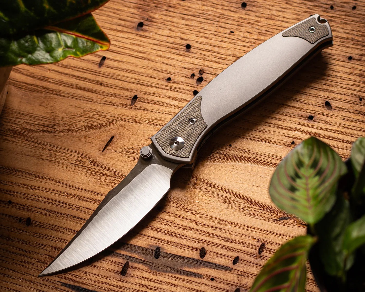 Folding knife with a curved stainless steel blade and a silver handle with textured grip insets on a wooden surface.