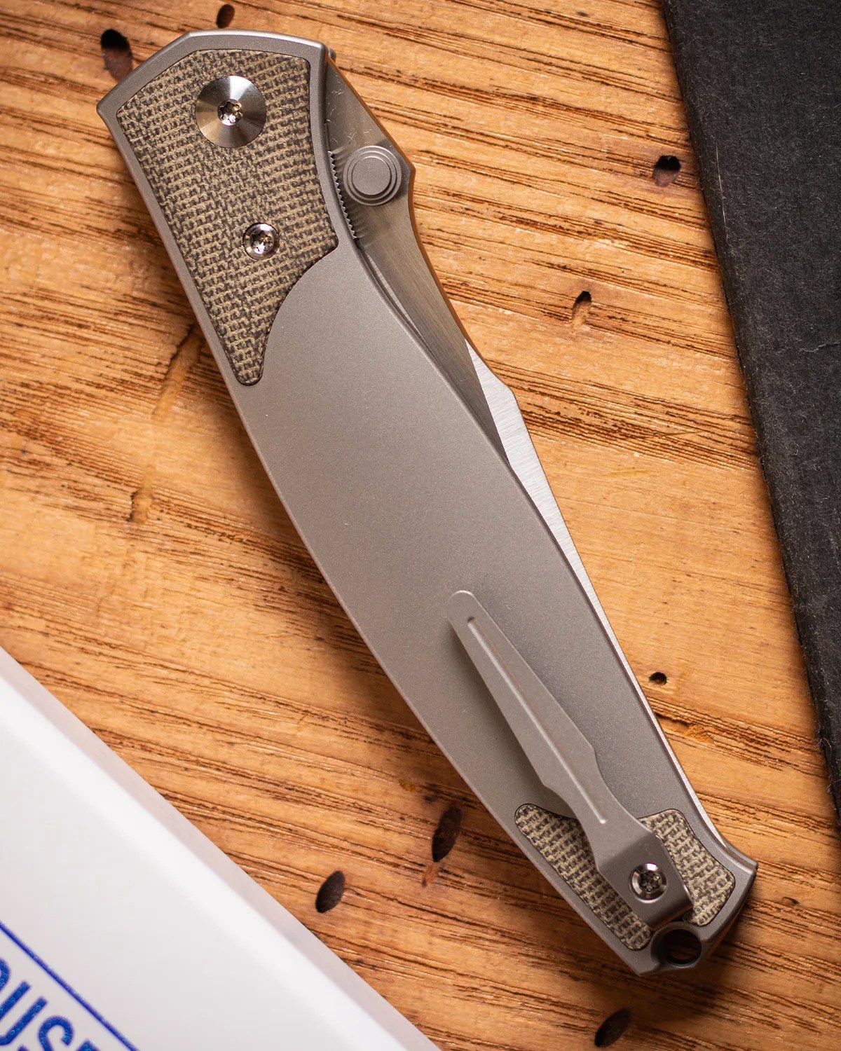 Closed folding pocket knife with a textured gray handle and metal clip on a wooden surface.