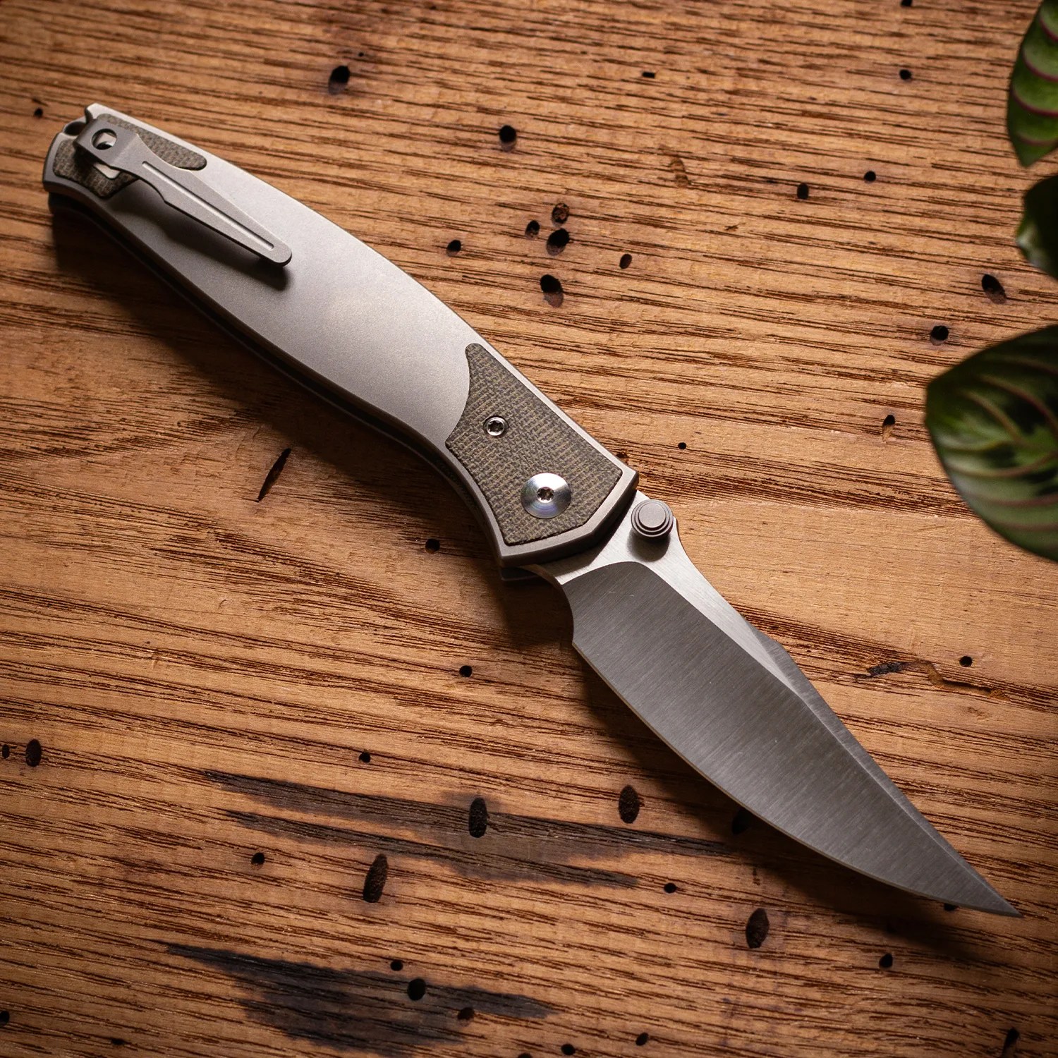 Folding knife with a silver blade and textured gray handle resting on a wooden surface.