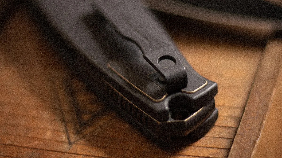 Close-up of a black metal nail clipper with a textured grip on a wooden surface.